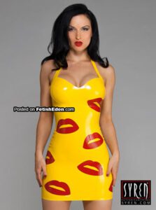 Sister Sinister wearing a yellow latex mini-dress with red lip prints and halter neckline, in a studio setting