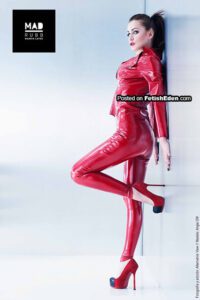 Girl poses in a red latex outfit featuring a fitted jacket and matching leggings, paired with red high heels.