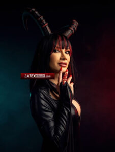 Devil Domme with red hair in a black wet-look outfit with dramatic devil horns in a dark, cinematic setting.