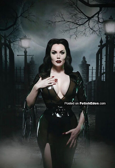 Morrigan Hel wearing a translucent olive latex dress in a gothic cemetery-like setting with mist, lamp posts, and iron gates.