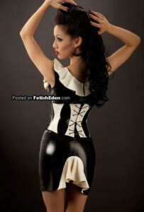 Jade Vixen posing in a glossy black and white latex mini-dress with a corset, white ruffle accents, and a retro-inspired hairstyle.