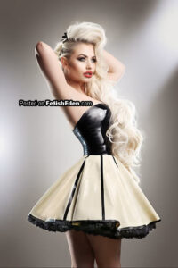 Fetish model with long platinum-blonde hair wearing a black and cream latex mini-dress in a studio portrait.